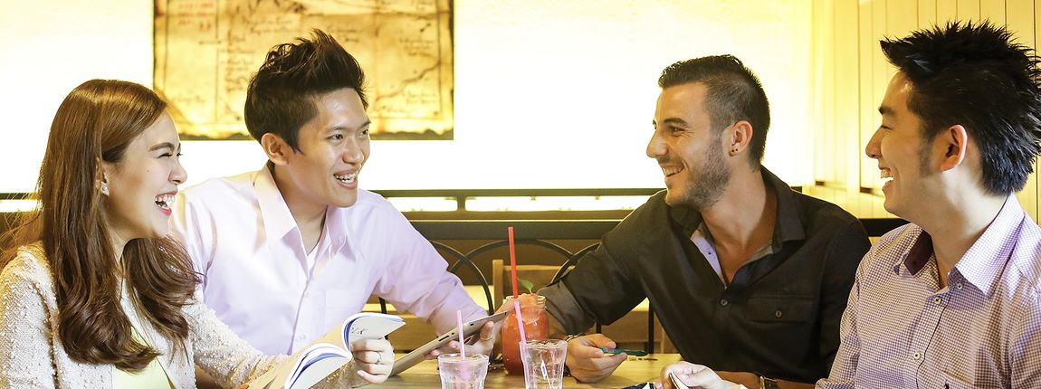 Four students talking and laughing over drinks in a campus café